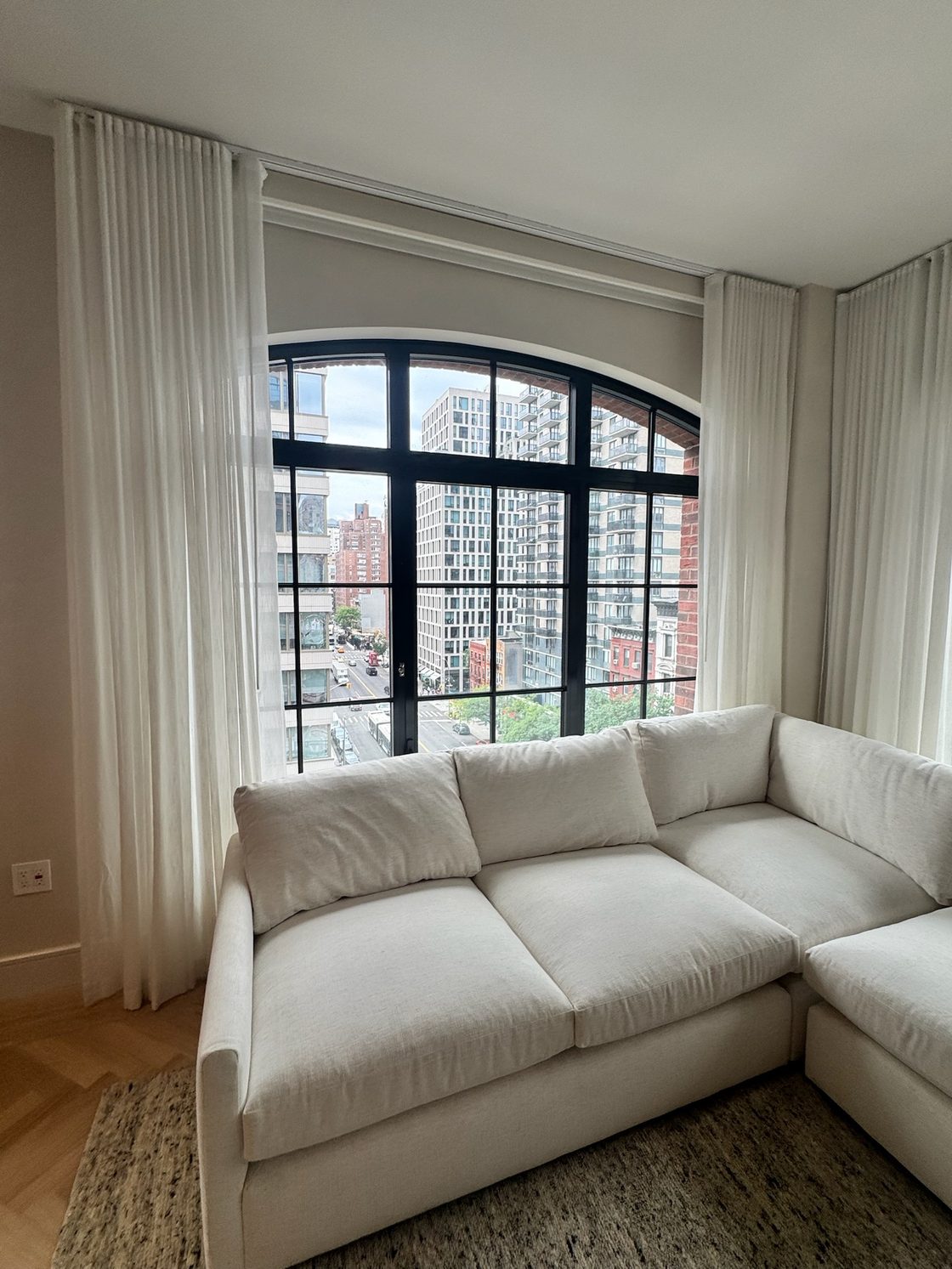 Sheer ripplefold drapery framing an arched steel window with a city view